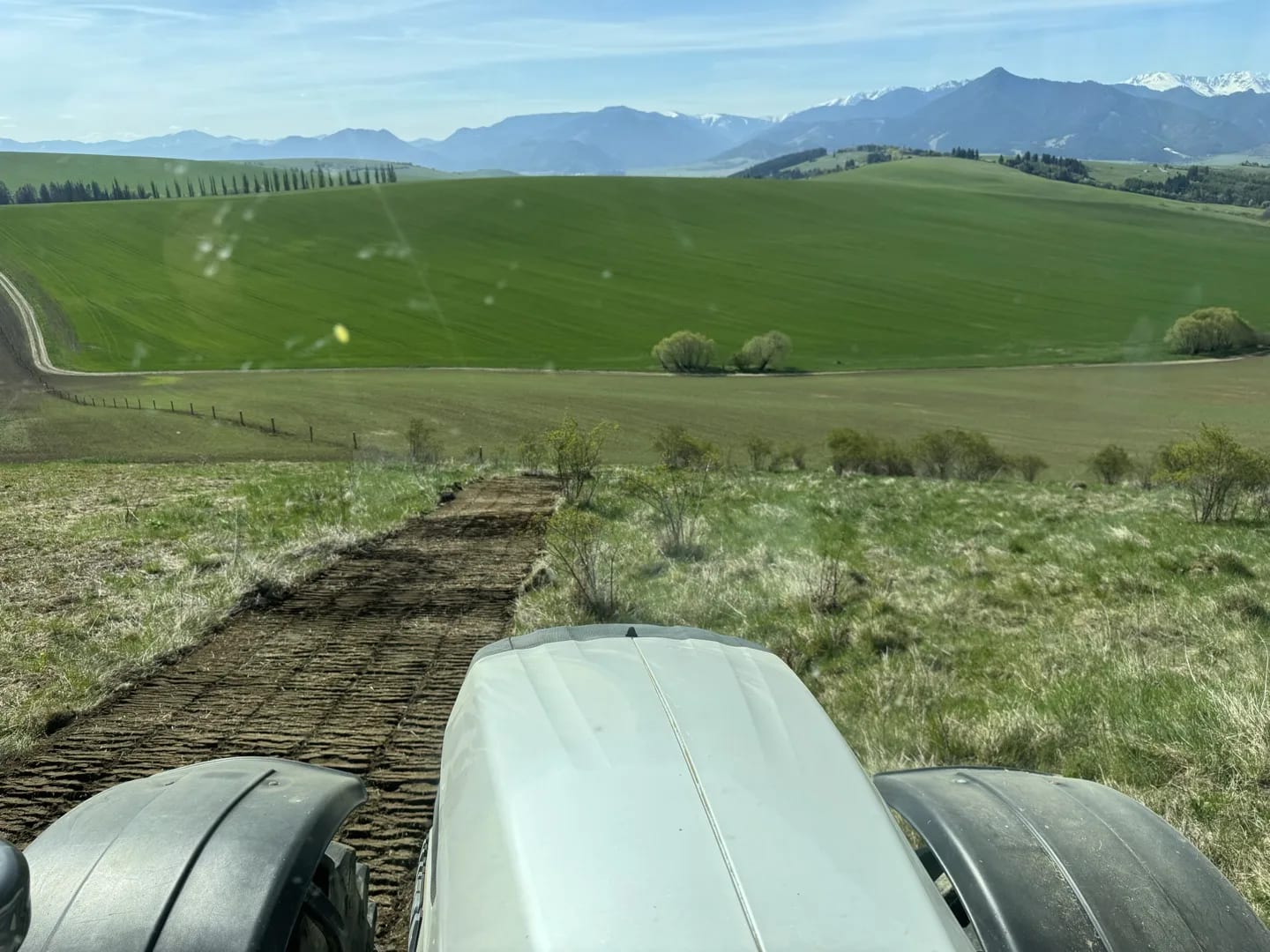 Kabína traktora Valtra T214 počas frézovania v Hajnicô. Výhľad cez kapotu na čerstvo vyfrézovaný pás pôdy s pohorím Tatier v pozadí.